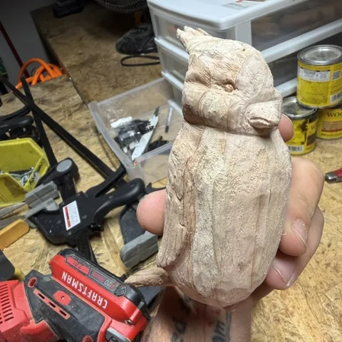 A carved owl in bare wood, held above the workbench