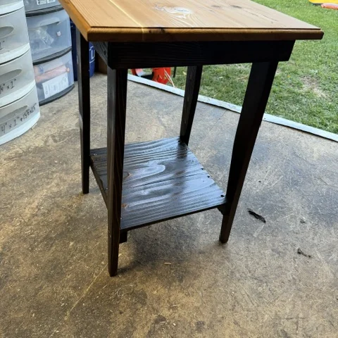 A finished side table outside, dark torched base under a natural top