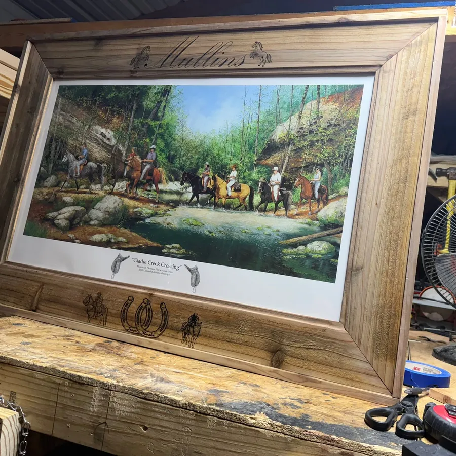 Custom-built wood picture frame with an engraved name across the top, on the workbench