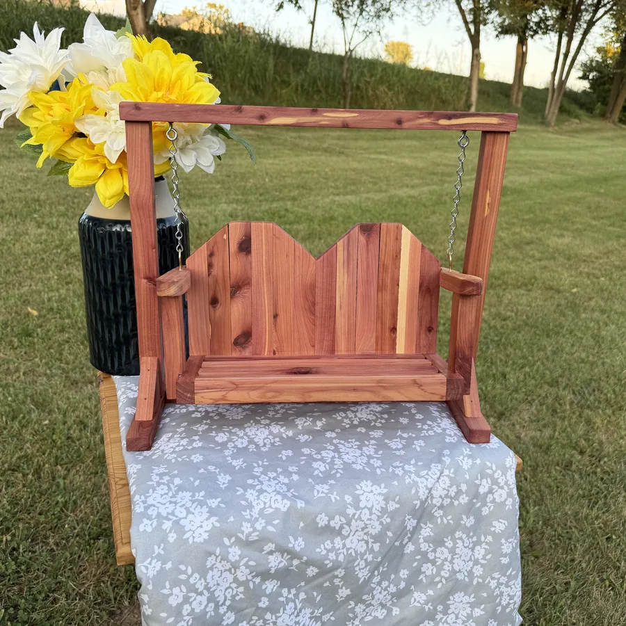 Handmade eastern red cedar loveseat swing with a scalloped back and arm rests, hanging by chain in its A-frame stand