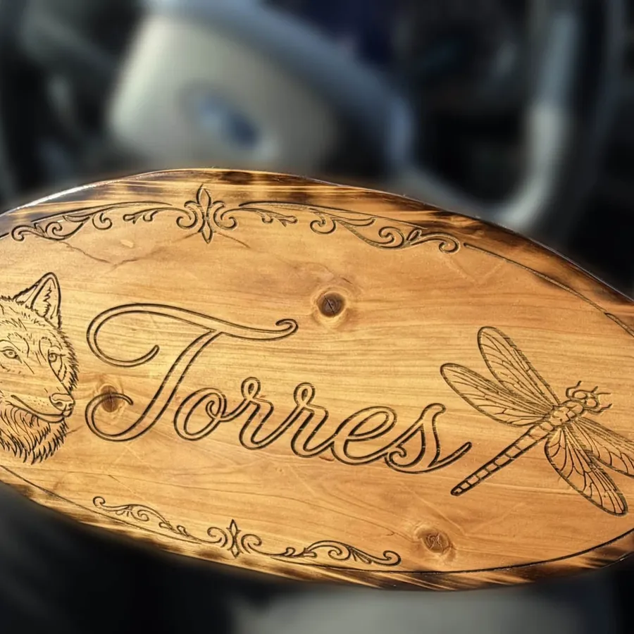 Engraved oval wood sign with a wolf, script lettering and a dragonfly, torch finished