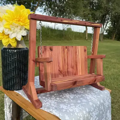 Mini porch swing in red cedar, hanging by chain in its A-frame stand