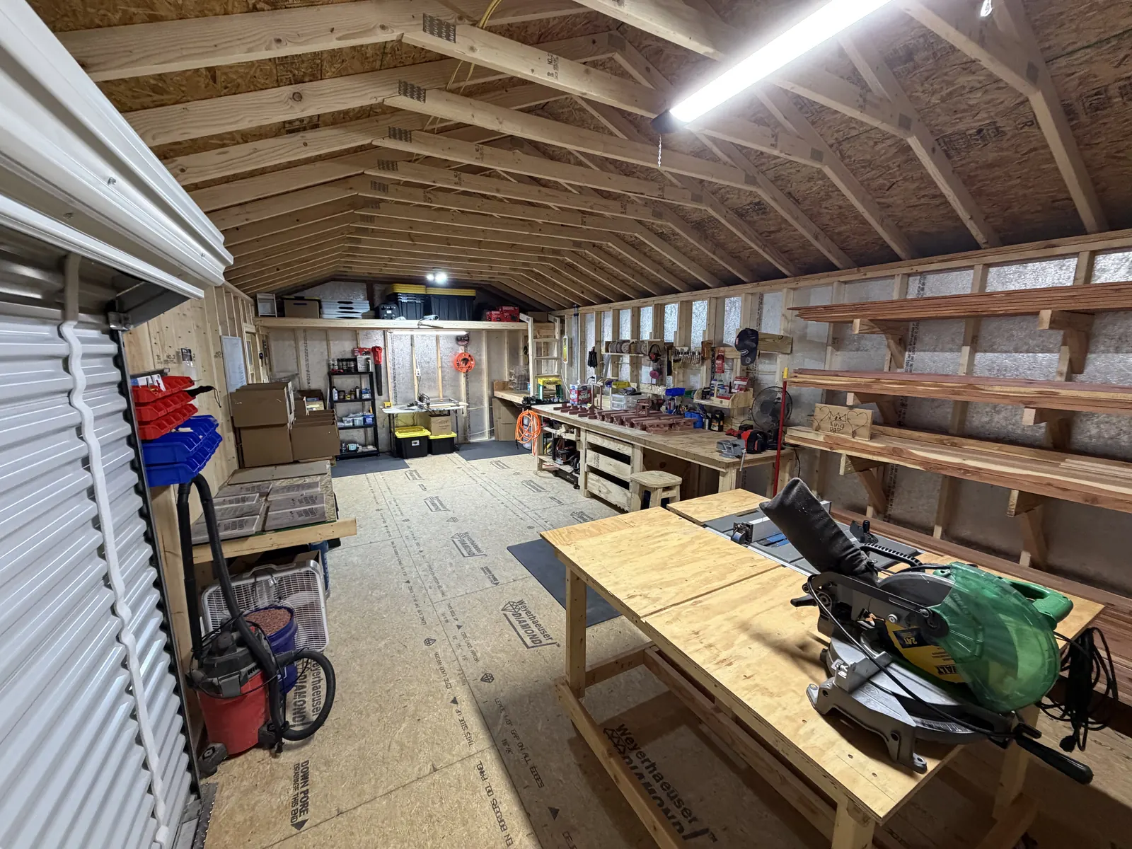 Harley's rebuilt workshop: workbenches down both sides, the miter saw station, and racks of cedar lumber along the wall