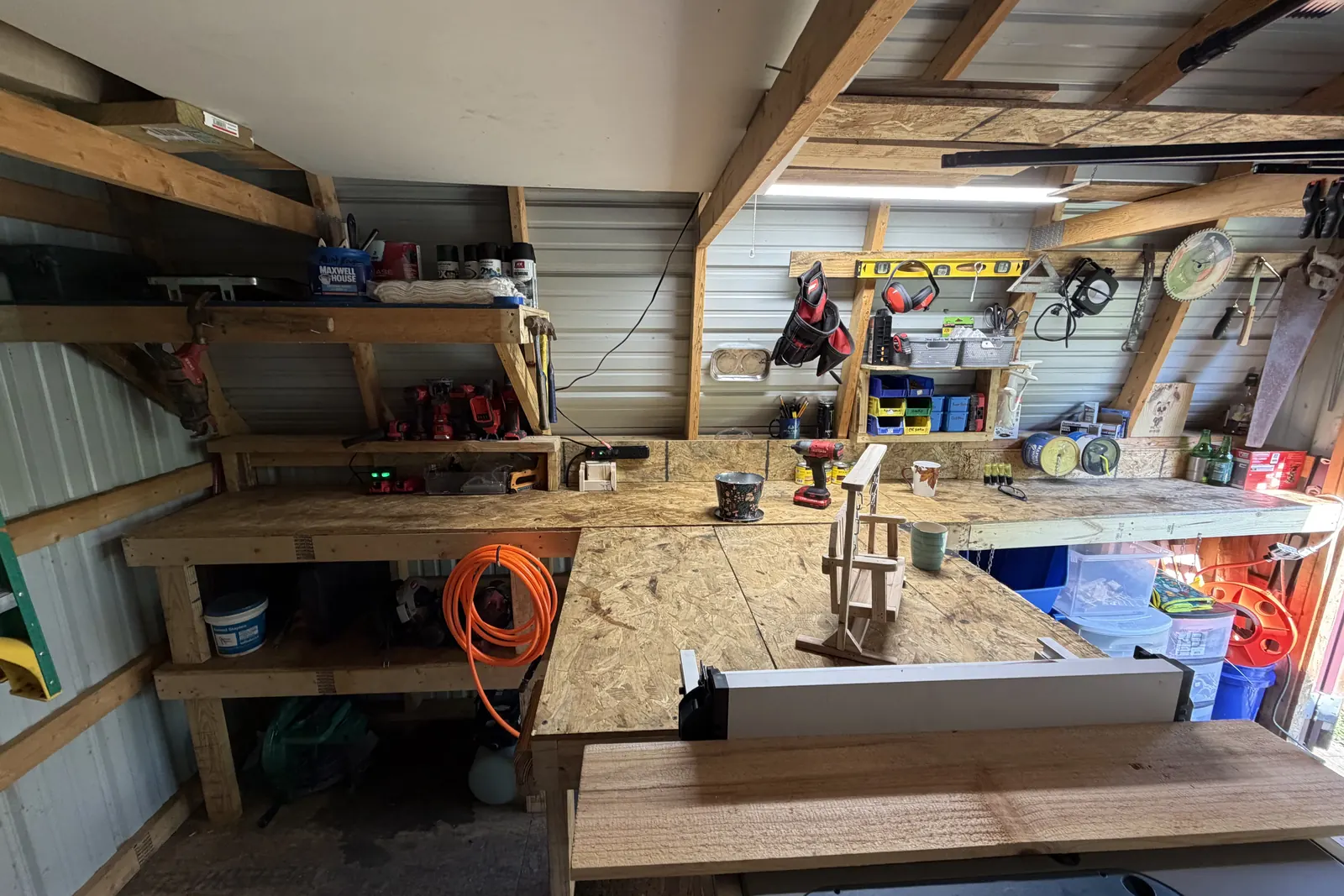 The workbench run in Harley's shop: a piece clamped mid-build, a driver beside it, shelves of finishes and tool batteries above.