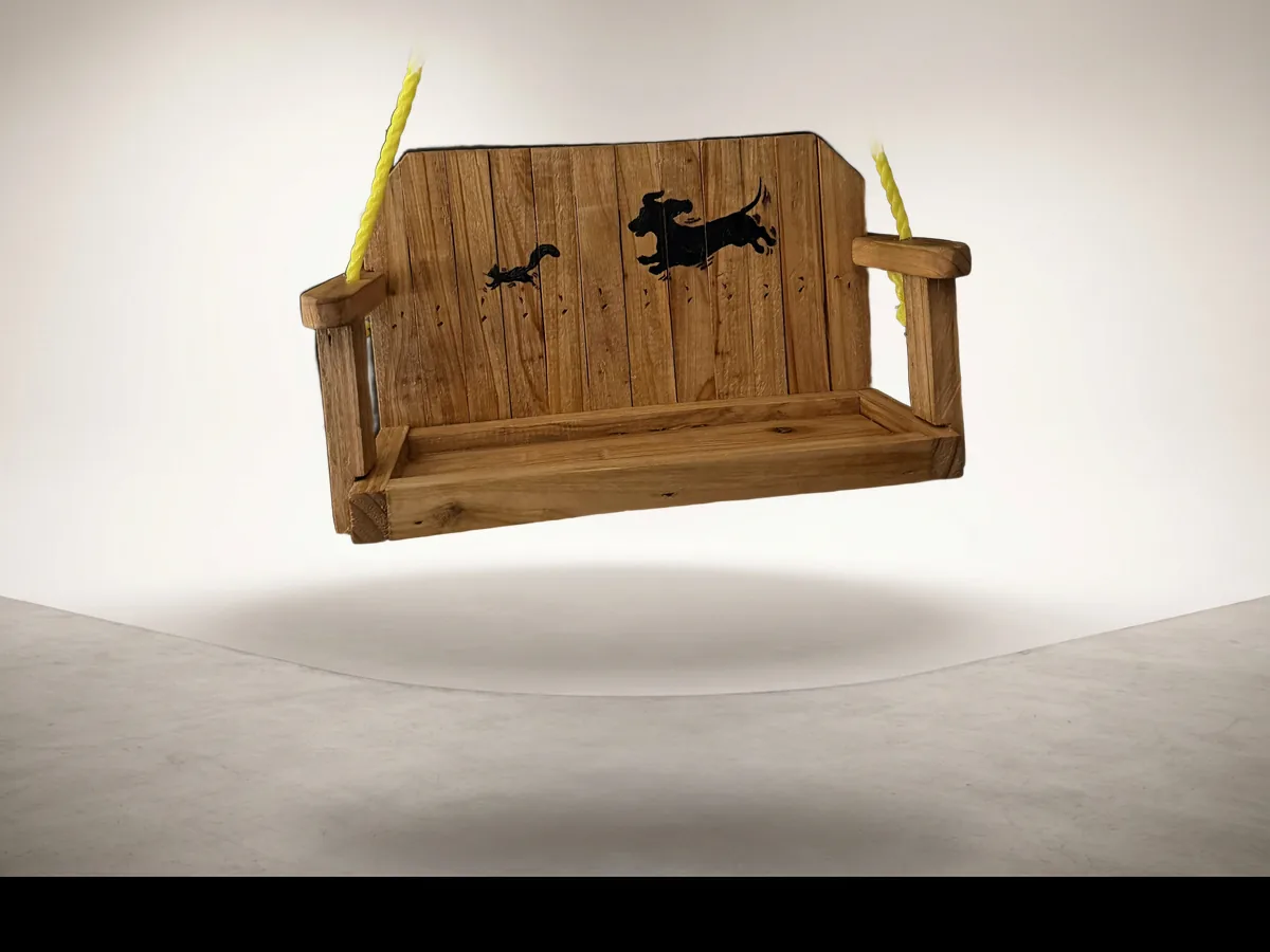 A cedar swing seat with a dachshund chasing a squirrel burnt into the backrest, hung on yellow rope, photographed on a clean studio backdrop.